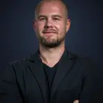 Porträt von Jan Jatzkowski, Gründer von Jatzkowski Solutions, mit verschränkten Armen vor dunklem Hintergrund