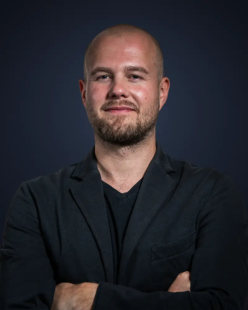 Porträt von Jan Jatzkowski, Gründer von Jatzkowski Solutions, mit verschränkten Armen vor dunklem Hintergrund